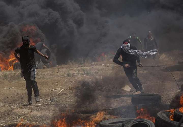 Dos palestinos corren en busca de refugio durante los enfrentamientos surgidos tras las protestas convocadas cerca de la frontera con Israel en el este de la franja de Gaza, hoy, 14 de mayo de 2018. EFE