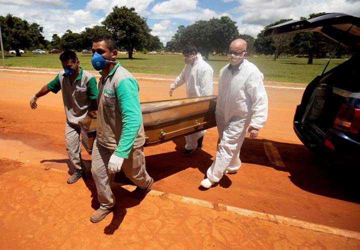 Trabajadores cargan un féretro con una víctima mortal de covid-19 rumbo a su entierro hoy, en el cementerio Campo da Esperança, en Brasilia. EFE