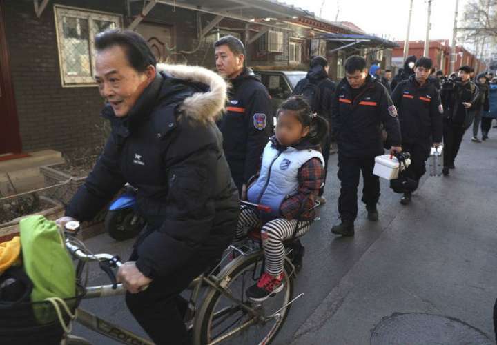 Un hombre lleva una niña en bicicleta junto a los investigadores en el exterior de la escuela elemental número 1 de Beijing en Xuanwu, en Beijing, China. AP