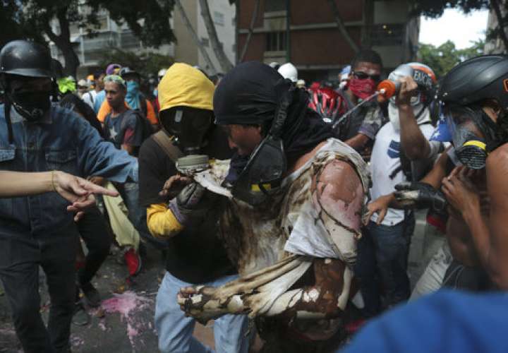 Un hombre es ayudado por manifestantes contra el gobierno después de que se quemó cuando los manifestantes prendieron fuego a una moto de la Guardia Nacional Bolivariana.  /  Foto: AP