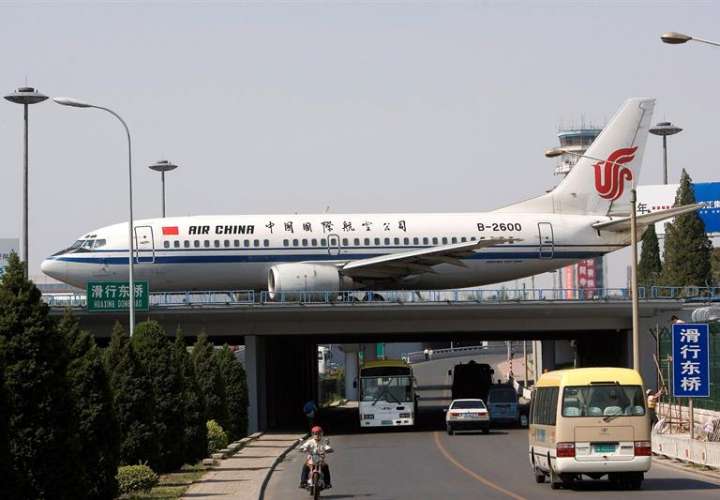 Un avión de las aerolineas Air China circula por una pista de aterrizaje mientras otros vehículos lo hacen por una autopista, en Pekín, China. EFE/Archivo