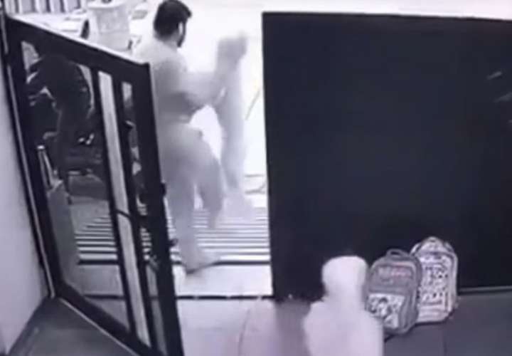 El en video se observa a una mujer parada en la puerta de su casa el autobús escolar mientras sostiene a su hijo en brazo y su niña permanece a un lado.