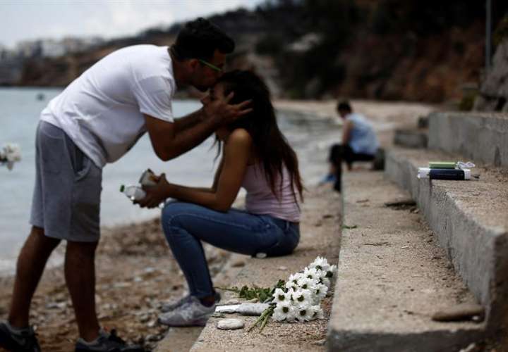 Un hombre besa a su hermana mientras un ramo de flores yace en el lugar donde un bebé de seis meses perdió la vida tras el incendio forestal de Mati, al noreste de Atenas (Grecia).  EFE