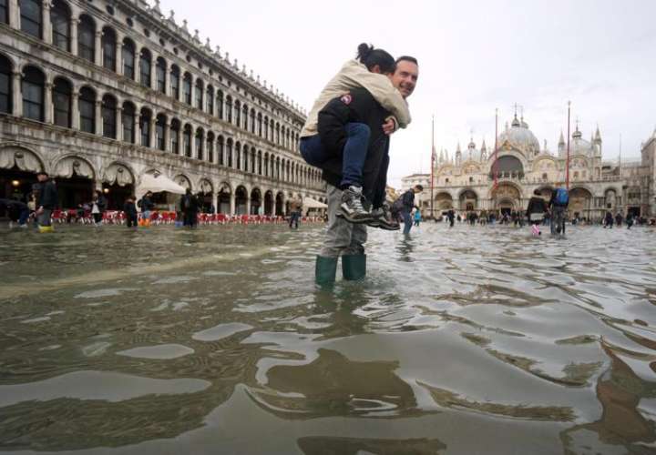 Un hombre carga a sus espaldas con su hija en la Plaza de San Marco, inundada como consecuencia del temporal de lluvia registrado en Venecia. EFE