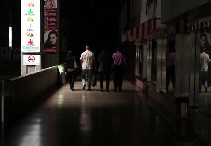 Un grupo de personas camina por un local comercial a oscuras por el apagón eléctrico en Caracas (Venezuela). EFE