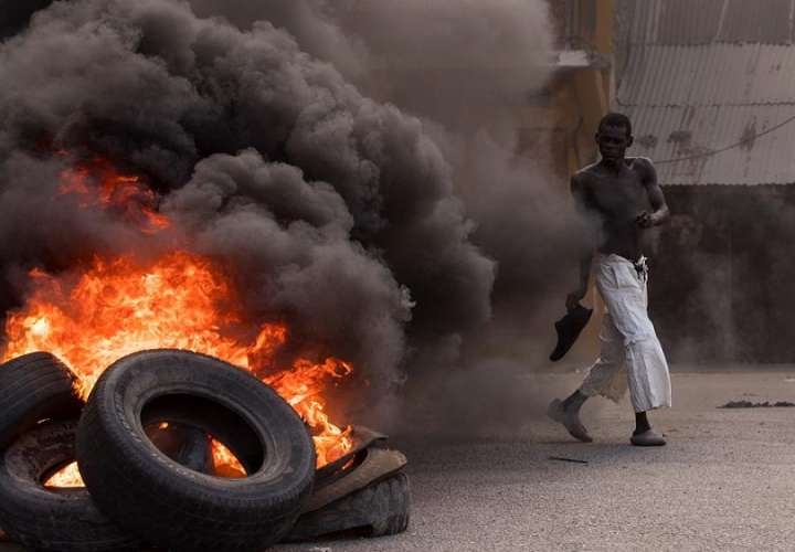 Un hombre camina frente a una pila de llantas en llamas durante una jornada de protestas a la vez que se rindieron homenajes al asesinado presidente Jovenel Moise, hoy, en Cap-Haitien (Haití). EFE