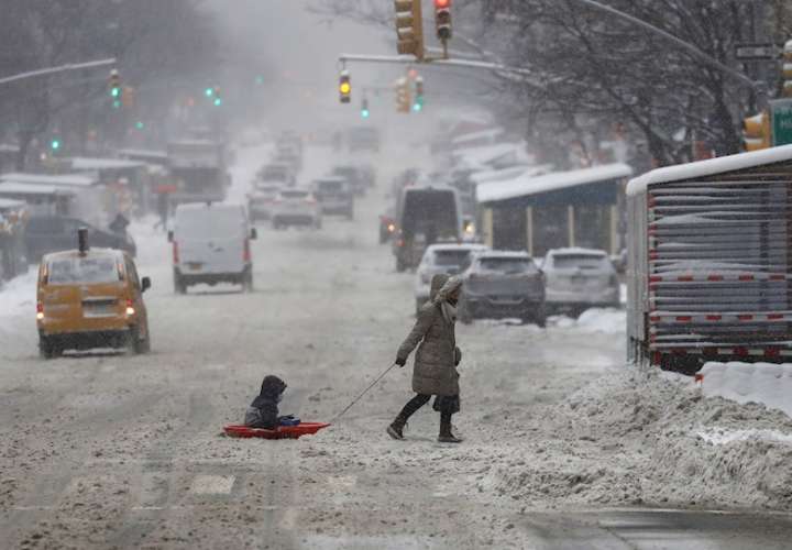 Una mujer y un niño sobre un trineo fueron registrados este sábado al cruzar una calle cubierta de nieve en Nueva York (NY, EE.UU.). EFE