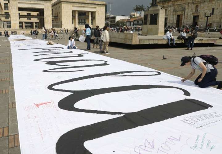 Personas escriben mensajes sobre una tela durante la conmemoración de los seis años de la firma del Acuerdo de Paz entre el Gobierno colombiano y las FARC en la Plaza de Bolívar, en Bogotá. Foto Archivo EFE