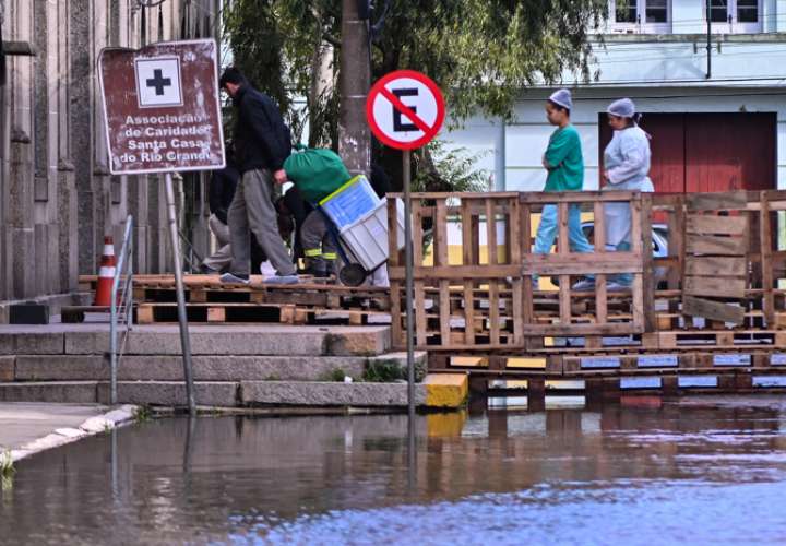 Empleados del Hospital Santa Casa caminan sobre un puente improvisado en medio a una zona inundada, este martes en el municipio de Rio Grande, estado de Rio Grande do Sul (Brasil). EFE