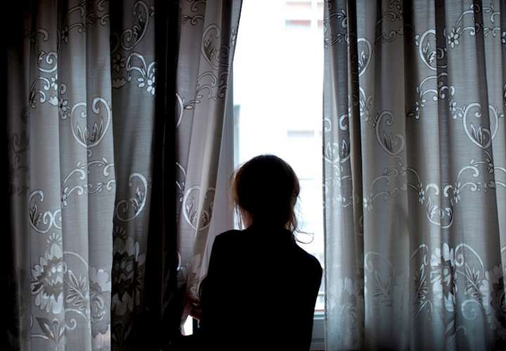 Una mujer observa a través de la ventana de su vivienda, en foto de archivo. EFE