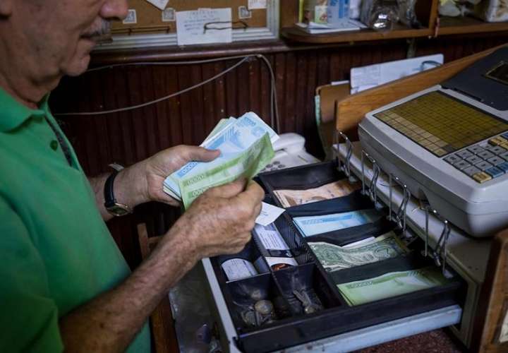 Una persona maneja una caja registradora en un local comercial con moneda venezolana y dólares estadounidenses. EFE