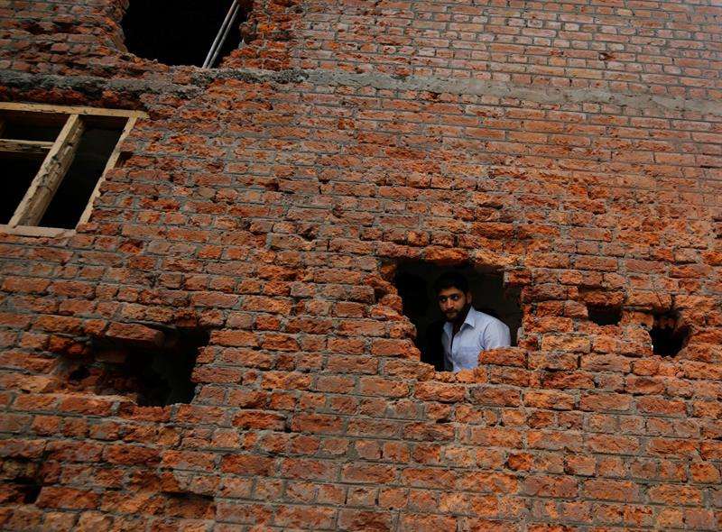 Un hombre se asoma por un agujero en la fachada de una vivienda que resultó dañada durante un tiroteo entre rebeldes y paramilitares indios en Srinagar, capital estival de la Cachemira india. EFE