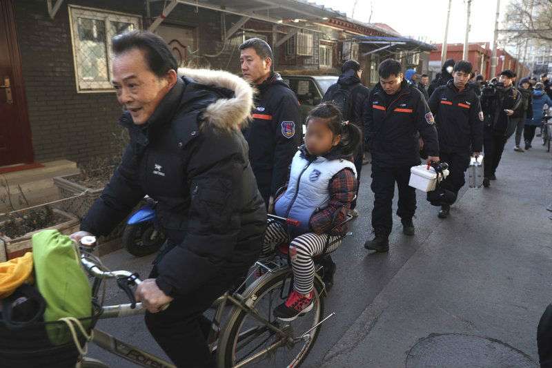 Un hombre lleva una niña en bicicleta junto a los investigadores en el exterior de la escuela elemental número 1 de Beijing en Xuanwu, en Beijing, China. AP