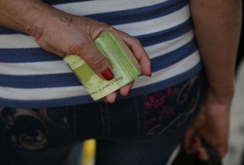 Una mujer sostiene un fajo de billetes para pagar su pasaje de autobús en Caracas, Venezuela. AP