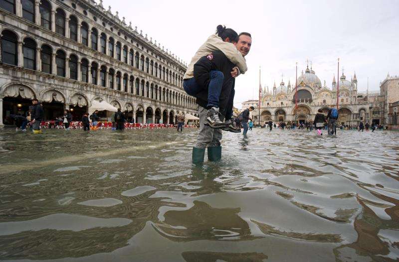 Un hombre carga a sus espaldas con su hija en la Plaza de San Marco, inundada como consecuencia del temporal de lluvia registrado en Venecia. EFE