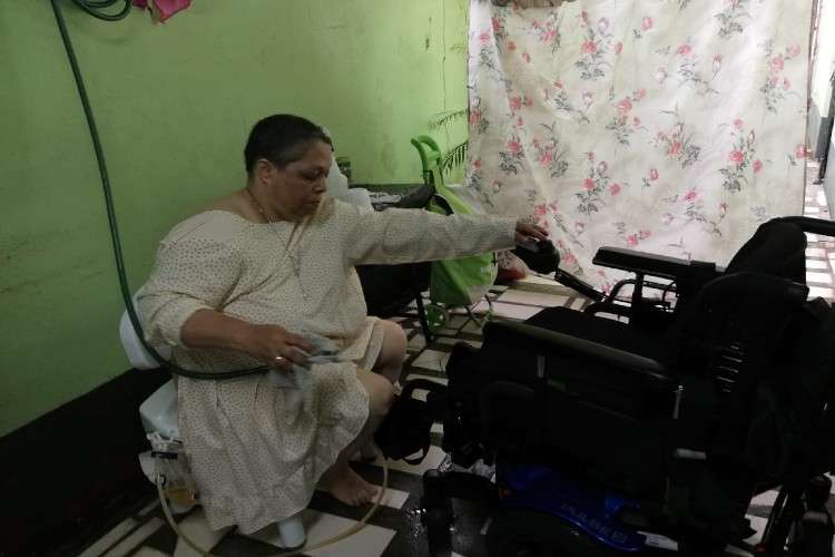 La hermana Ana Fisher mientras desinfecta la silla de ruedas en el baño improvisado fuera de su casa. Imagen: Cortesía