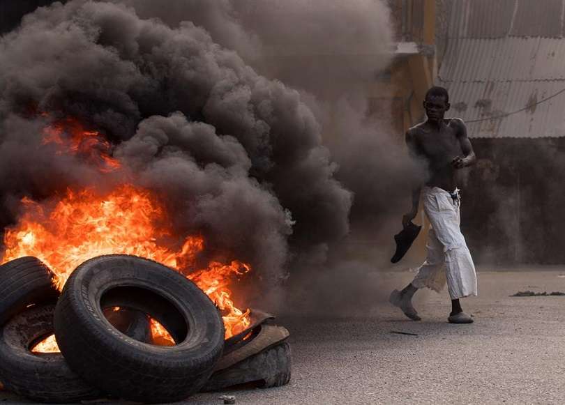 Un hombre camina frente a una pila de llantas en llamas durante una jornada de protestas a la vez que se rindieron homenajes al asesinado presidente Jovenel Moise, hoy, en Cap-Haitien (Haití). EFE