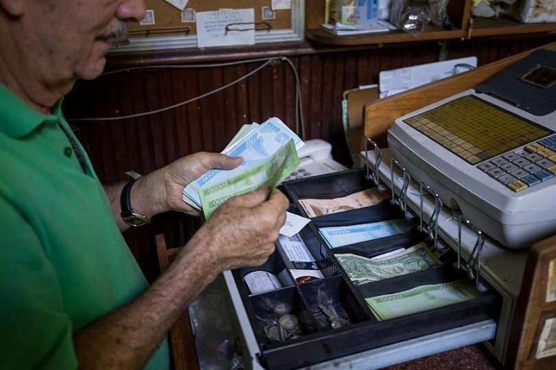 Una persona maneja una caja registradora en un local comercial con moneda venezolana y dólares estadounidenses. EFE